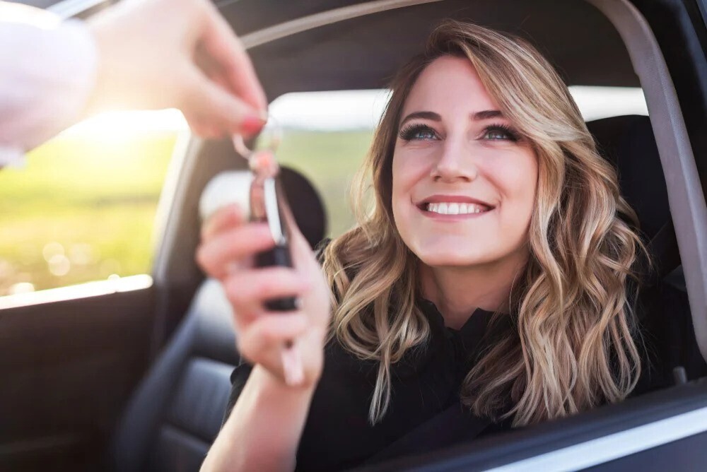 Smiling international student with the car key in their newly leased car.