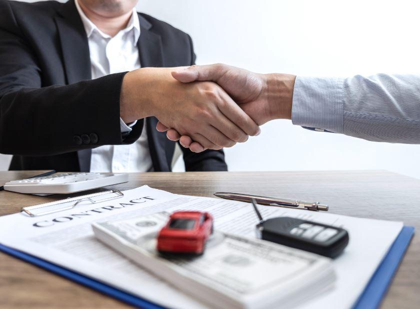 A person signing an Auto Bandit car lease agreement, with a stack of cash in his hand.