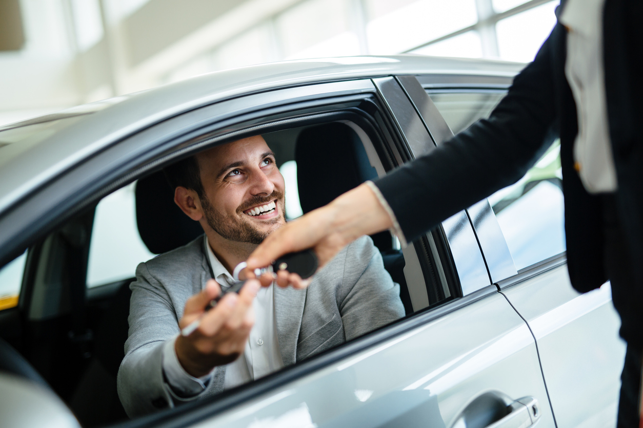 Smiling man receives keys for his new car.